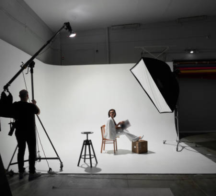 Fashion photography in a photo studio. Professional male photographer taking pictures of beautiful woman model on camera, backstage