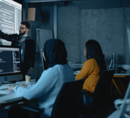 Teacher Giving Computer Science Lecture to Diverse Multiethnic Group of Female and Male Students in Dark College Room. Projecting Slideshow with Programming Code. Explaining Information Technology.