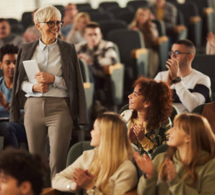 Large group of happy college students applauding to their senior female professor in a lecture hall.